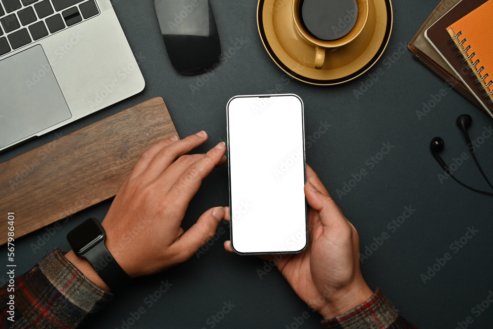 Overhead view of hipster man hands holding smart phone while sitting front of laptop at workstation Overhead view of hipster man hands holding smart phone while sitting front of laptop at workstation