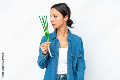 Young hispanic woman holding chive isolated on white background looking to the side