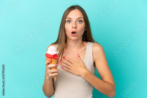 Young Lithuanian woman with cornet ice cream isolated on blue background surprised and shocked while looking right