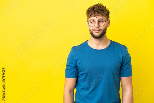 Young handsome caucasian man isolated on yellow background having doubts while looking side