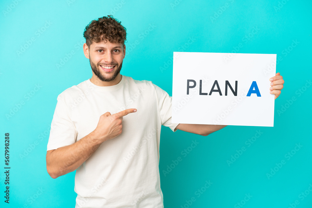 Young handsome caucasian man isolated on blue background holding a placard with the message PLAN A and pointing it Young handsome caucasian man isolated on blue background holding a placard with the message PLAN A and pointing it
