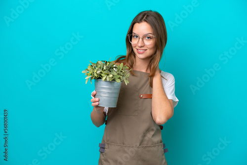 Young caucasian gardener woman holding a plant isolated on blue background laughing