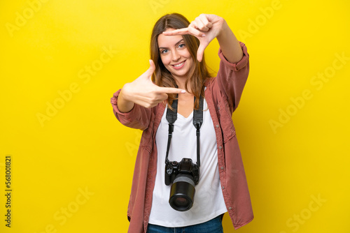 Young photographer caucasian woman isolated on yellow background focusing face. Framing symbol