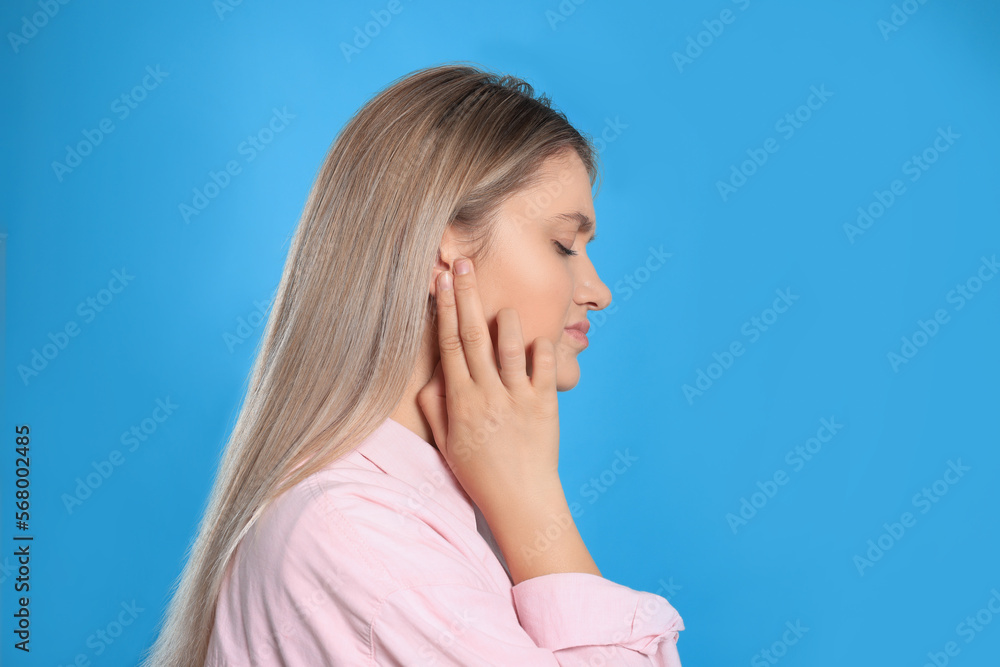 Young woman suffering from ear pain on light blue background. Space for text Young woman suffering from ear pain on light blue background. Space for text