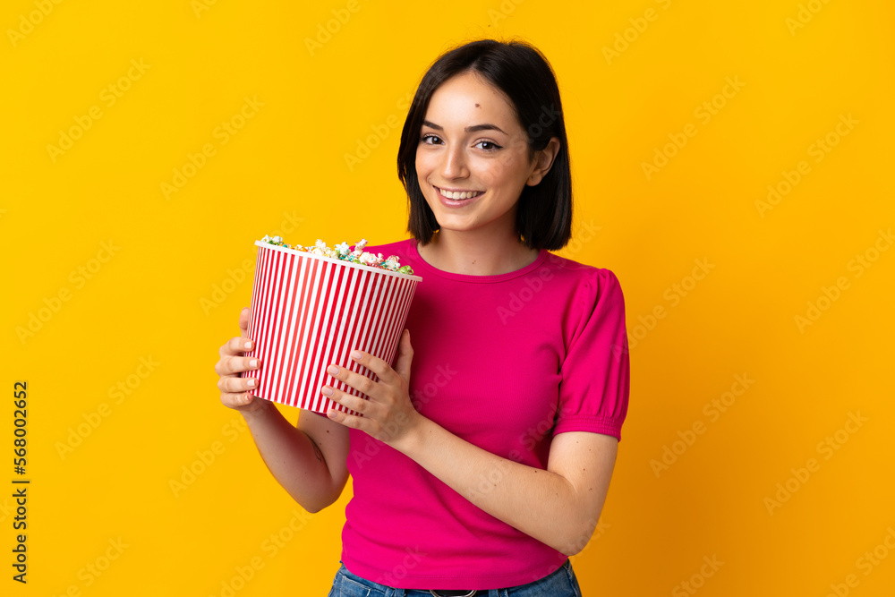 Young caucasian woman isolated on yellow background holding a big bucket of popcorns Young caucasian woman isolated on yellow background holding a big bucket of popcorns