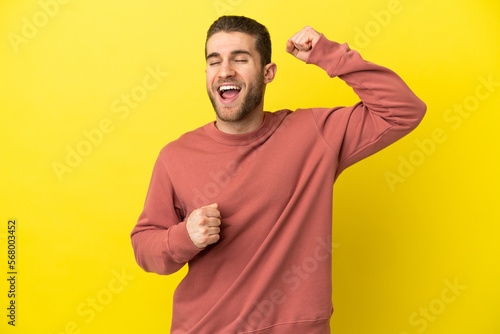 Handsome blonde man over isolated yellow background celebrating a victory