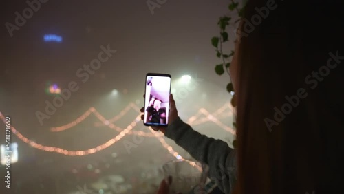Happy woman with the glass of sparkling champagne in hands having video call with family or friends and cheering, woman with smartphone in hands on amazing festive background at night, dancing woman