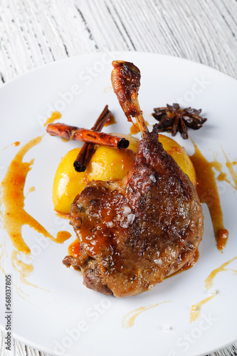 Close-up duck leg Confit with apples in orange sauce on a white plate.
