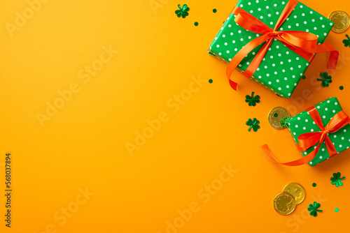 St Patrick's Day concept. Top view photo of green present boxes with orange ribbon bows gold coins and clover shaped confetti on isolated yellow background with empty space