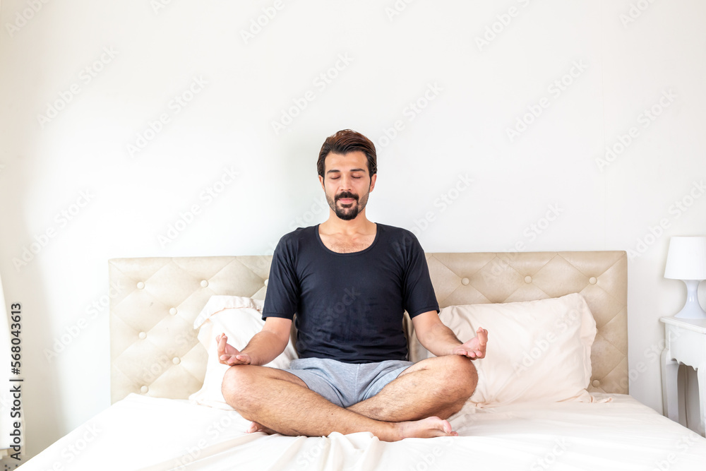 Man meditating while sitting on bed in morning. Young man doing yoga in bed. Male meditating on bed at home. Meditate on the bed before sleep. Man meditating while sitting on bed in morning. Young man doing yoga in bed. Male meditating on bed at home. Meditate on the bed before sleep.