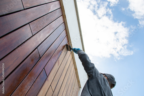 Restoration of hardwood facade siding, dramatic low angle view, woodworker applying pigment oil with brush