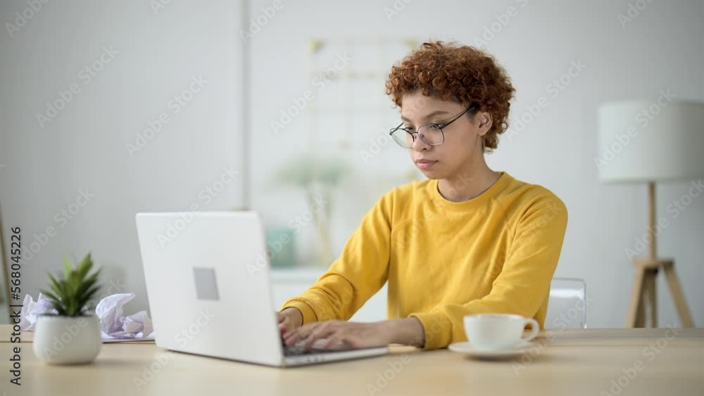 Young woman sits in home office at workplace and engaged online freelance work. Concentrated, businesslike and serious girl. Self-employed professional activity, fulfill order. Type text on keyboard. Young woman sits in home office at workplace and engaged online freelance work. Concentrated, businesslike and serious girl. Self-employed professional activity, fulfill order. Type text on keyboard.