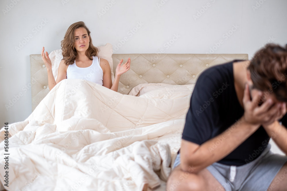 Young couple having problems with sex life. Couple quarreling and fighting in relationship at home. Relationship problems. Man sitting on the edge of the bed in bedroom. Young couple having problems with sex life. Couple quarreling and fighting in relationship at home. Relationship problems. Man sitting on the edge of the bed in bedroom.