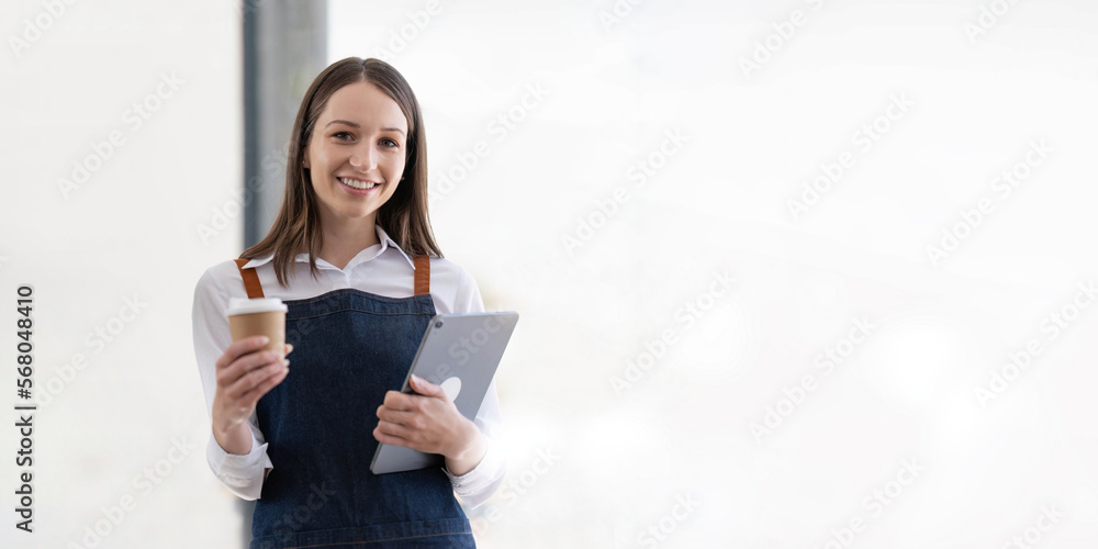 Beautiful asian young barista woman in apron holding tablet and cup standing in front of the door of cafe with open sign board. Business owner startup SME entrepreneur concept Beautiful asian young barista woman in apron holding tablet and cup standing in front of the door of cafe with open sign board. Business owner startup SME entrepreneur concept