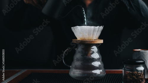 Professional barista making filtered drip coffee in coffee shop. Close up of hands barista brewing a drip hot espresso, pour over coffee with hot water and filter paper in cafe. photo