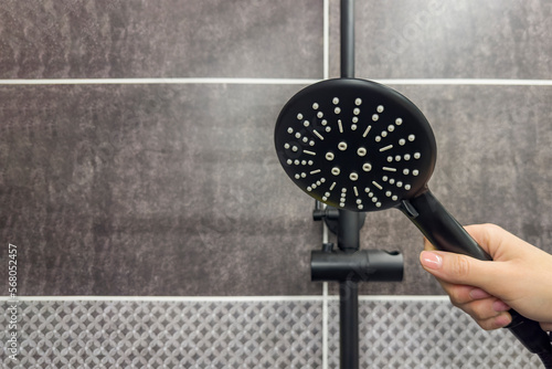 Close-up of a wall mounted hand shower, a hand holds a black colored shower head. The concept of repairing plumbing, cleaning or cleaning the shower room. Place for text or copy space