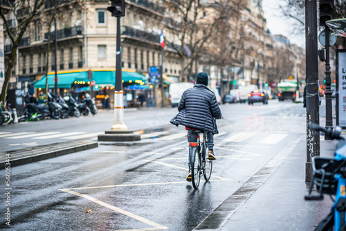 Active Lifestyle in Paris: Man Cycling on a Rainy Day through the Charming Old City Streets with Wet Pavement, Wearing a Jacket from the Back © ArtyomPoly's