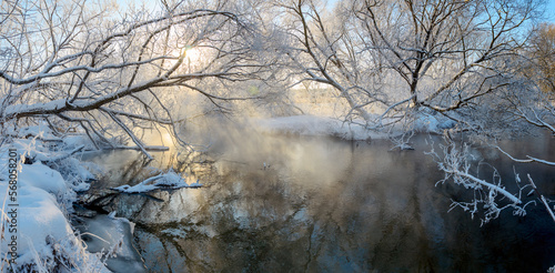 Winter sunny panoramic landscape with bare trees and forest river.Sun shining through the tree branches and fog rising from water. © valeriy boyarskiy