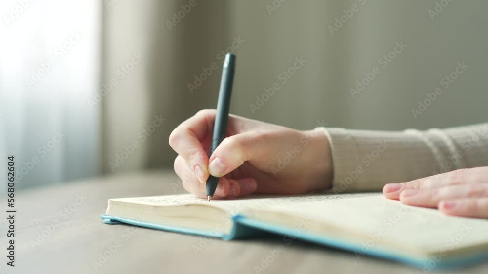 close-up of a female hands taking notes in a notebook notepad using pen on modern desk at home young woman writes in a diary with a pen while sitting at the table Close up commonplace close-up of a female hands taking notes in a notebook notepad using pen on modern desk at home young woman writes in a diary with a pen while sitting at the table Close up commonplace