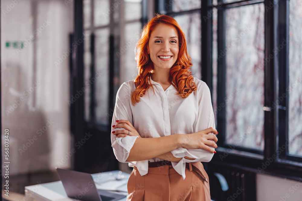Fototapeta premium Portrait of confident young businesswoman standing in office with arms crossed.