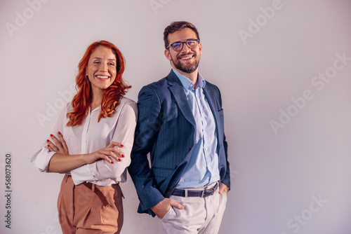 Business partners posing in front of gray background, looking at camera and smiling.