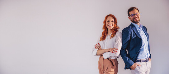 Business partners posing in front of gray background, looking at camera and smiling.