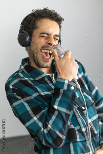 Mixed race man dressed in checked shirt singing into a condenser microphone