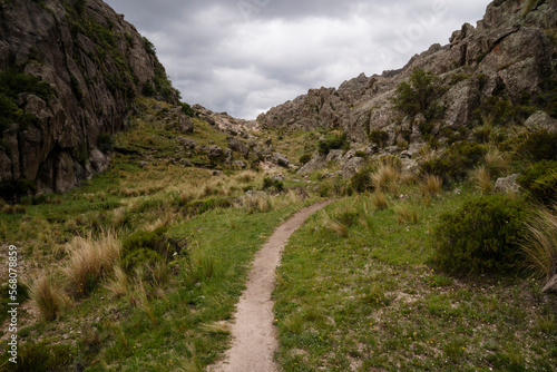 iew of the empty hiking path across the green grass and rocky hills in a cloudy early morning. 