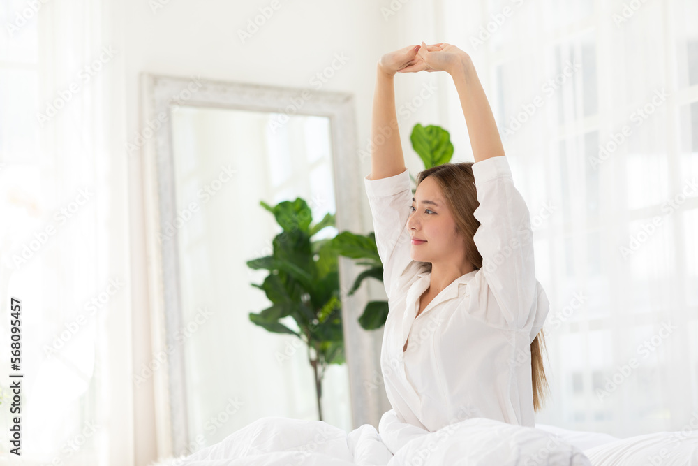 Beautiful Asian young Woman stretching her arm after wake up on bed and looking outside windows in cozy bedroom feeling so fresh and relax in the morning.Health care Concept Beautiful Asian young Woman stretching her arm after wake up on bed and looking outside windows in cozy bedroom feeling so fresh and relax in the morning.Health care Concept