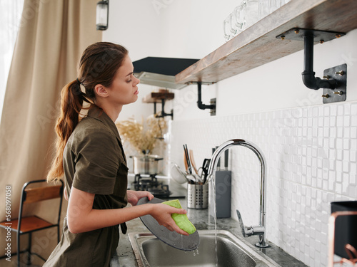 Woman tired and angry hands without gloves washes dishes with a dishwashing sponge with bubbles, household chores, no dishwasher, high water consumption. Stylish kitchen design