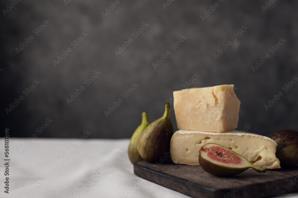 cheese and figs on a wooden board on a dark background