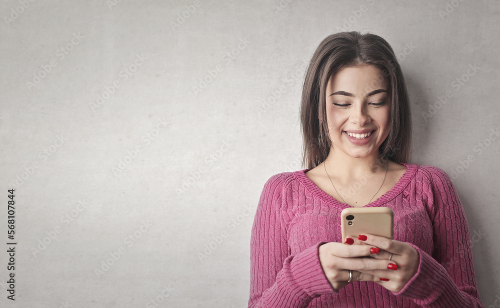 portrait of a young woman leaning against a gray wall while using a smartphone portrait of a young woman leaning against a gray wall while using a smartphone