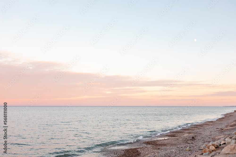 Pastel sunset on beach with tiny crescent moon