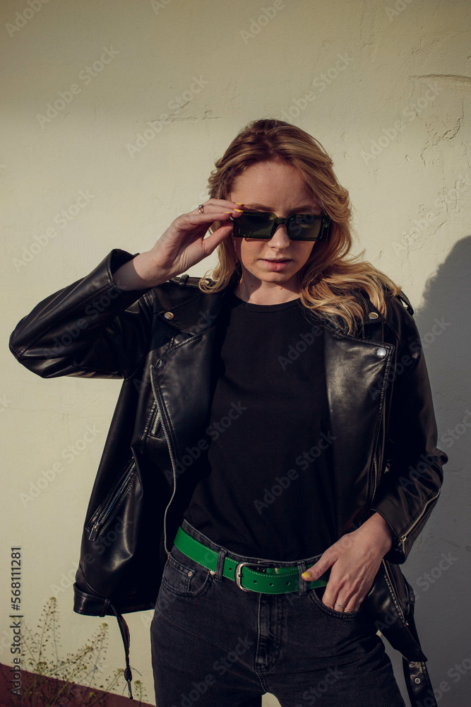 beautiful girl model with coffee in a black jacket in a black baseball cap on a chair sitting outside on the stairs posing for the camera with a phone in green clothes in sneakers fashion beautiful girl model with coffee in a black jacket in a black baseball cap on a chair sitting outside on the stairs posing for the camera with a phone in green clothes in sneakers fashion