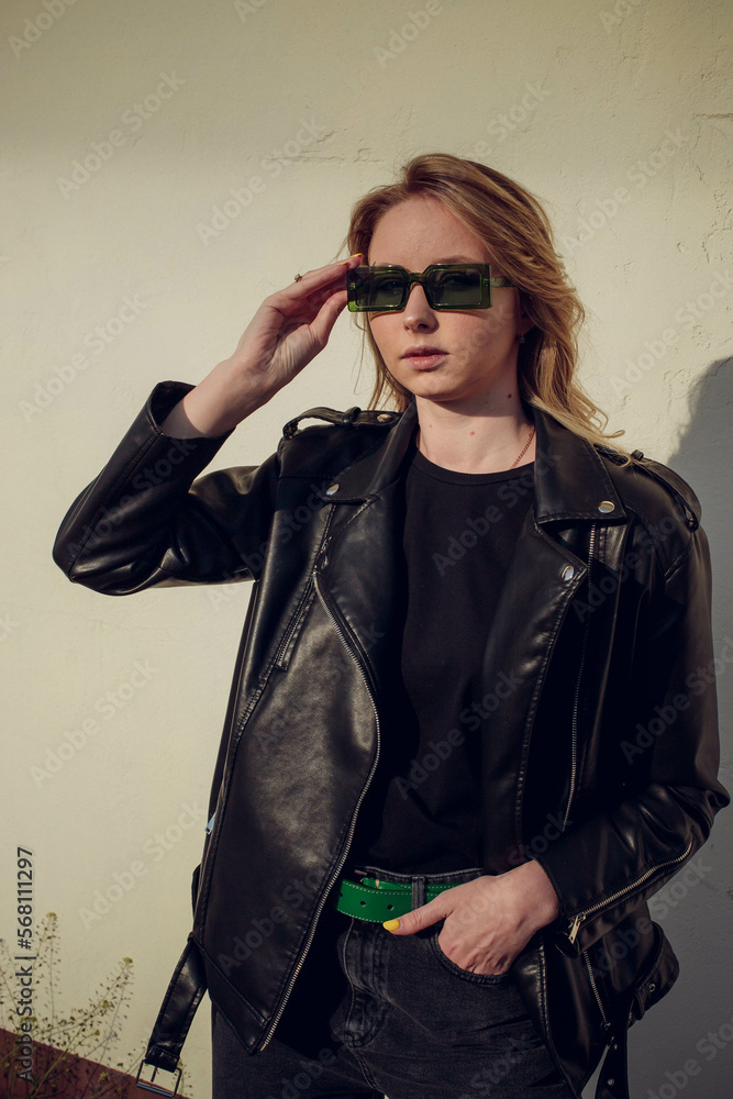 beautiful girl model with coffee in a black jacket in a black baseball cap on a chair sitting outside on the stairs posing for the camera with a phone in green clothes in sneakers fashion beautiful girl model with coffee in a black jacket in a black baseball cap on a chair sitting outside on the stairs posing for the camera with a phone in green clothes in sneakers fashion
