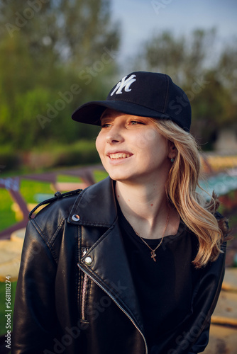 beautiful girl model with coffee in a black jacket in a black baseball cap on a chair sitting outside on the stairs posing for the camera with a phone in green clothes in sneakers fashion