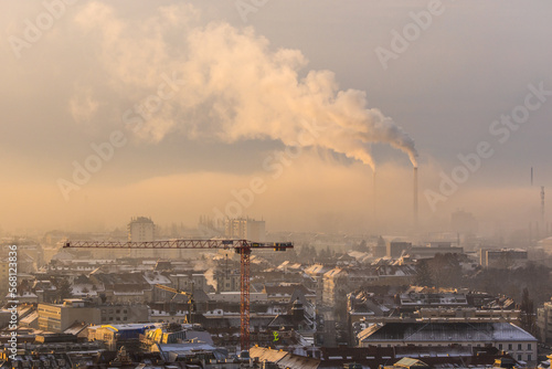 City view of Graz in Austria with buildings, cranes and an industrial plant with smoking chimneys on a foggy winter morning