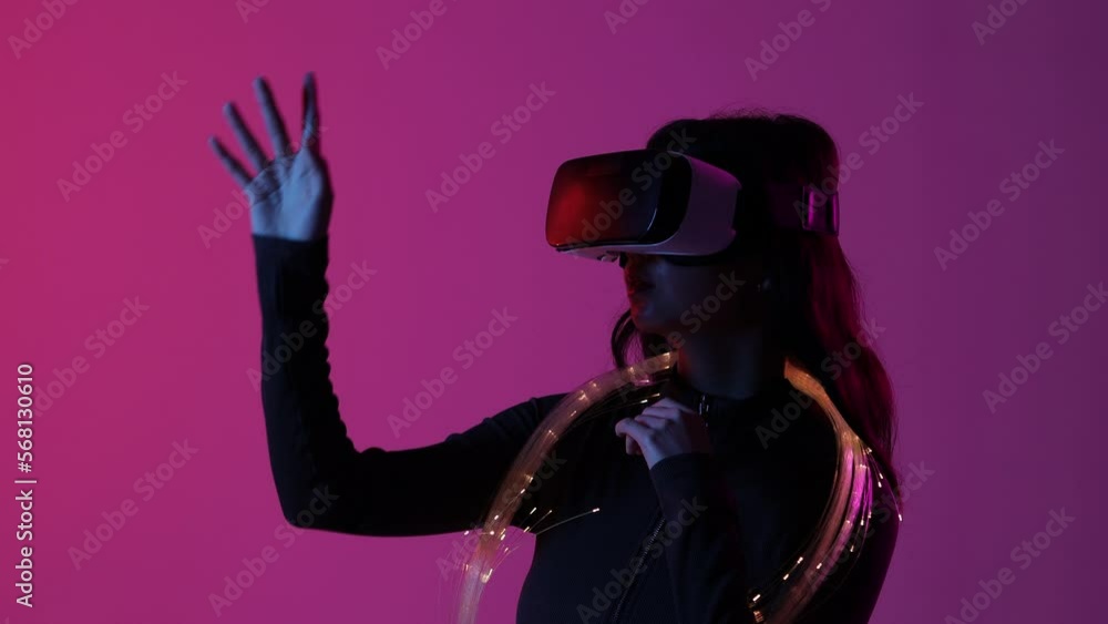 Woman in futuristic costume. Female in modern VR glasses interacting with network while having virtual reality experience. Augmented reality game, future technology, AI concept. VR. Neon light. Woman in futuristic costume. Female in modern VR glasses interacting with network while having virtual reality experience. Augmented reality game, future technology, AI concept. VR. Neon light.