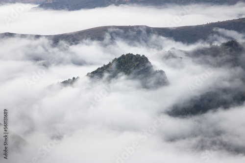 Photo of the peaks rock and hills covered trees in early Autumn on the background clouds and fog. Fog lies in the gorges and canyons but peaks see from a fog