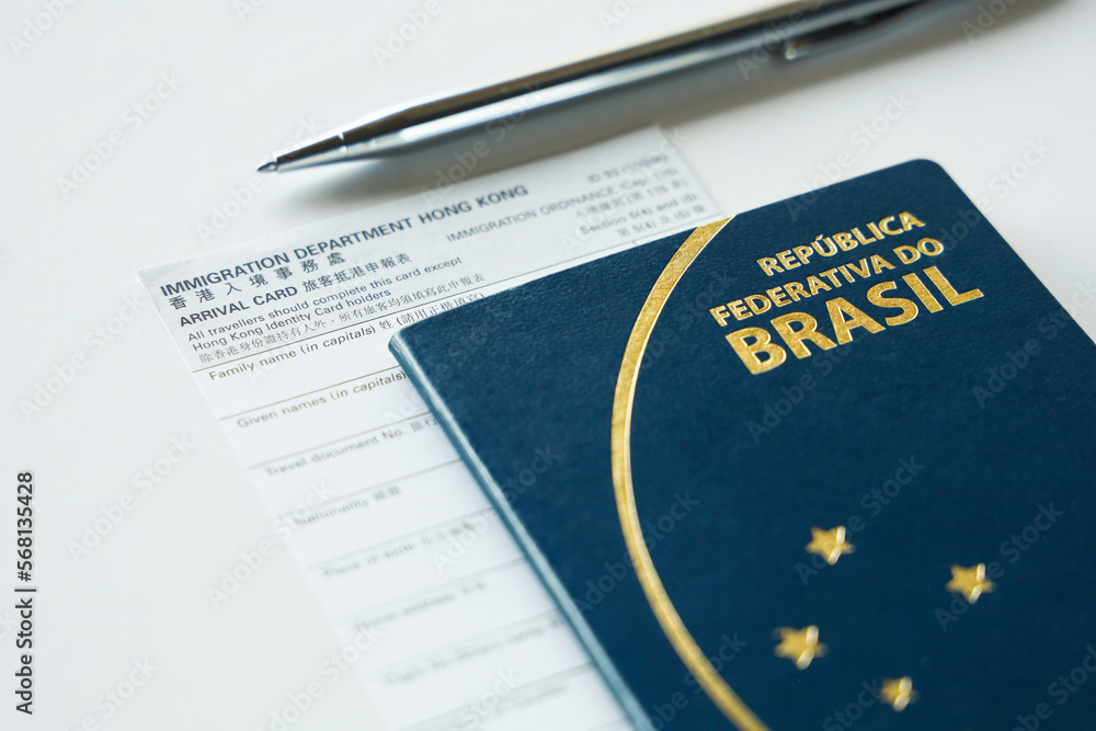 HONG KONG, CHINA, FEBRUARY 2020 - Tourist filling arrival card at Hong Kong immigration checkpoint at the airport. The scene shows an arrival card, a Brazilian passport and a ballpoint pen. - obrazy, fototapety, plakaty 