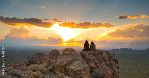 Two people sit and watch the desert sunset