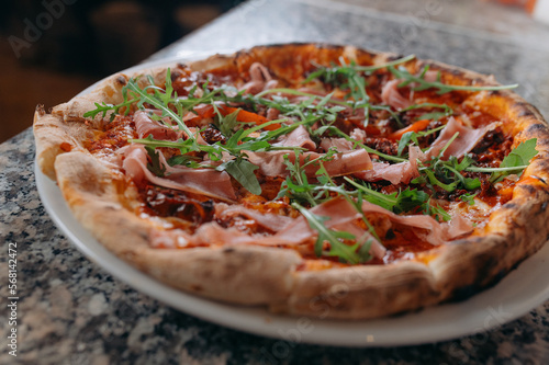 Pizza with prosciutto and rocket salad on wooden table.