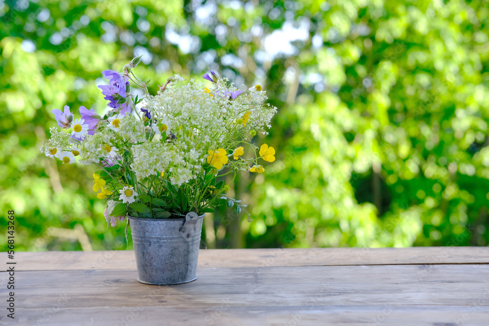 bouquet of wild flowers on table wooden table in garden, beautiful blurred natural landscape in background with green foliage and soft sunset transparenting through branches, concept cozy mood