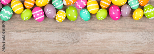 Colorful Easter egg top border. Overhead view on a light wood banner background. Copy space.