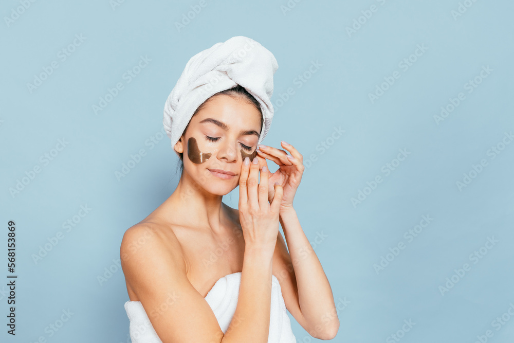 Young woman wearing towel applying eye patches Young woman wearing towel applying eye patches