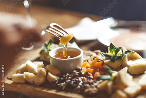 Cheese platter with different cheeses, nuts, honey, on rustic wooden background. Retro styled cheese variety selection on light wood board. High quality photo