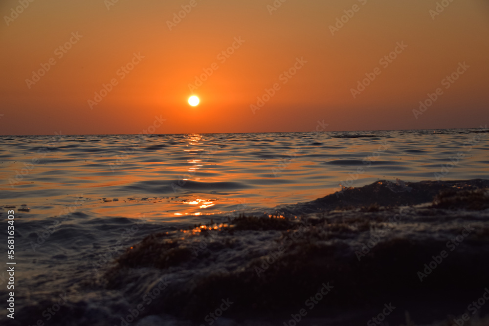 Obraz premium Vibrant sunset descending on the horizon, sea in golden colors, small waves gently touching the sands,