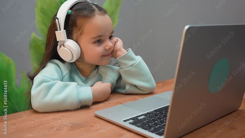 A little cute girl with white headphones watching a cartoon online on a laptop. A little cute girl with white headphones watching a cartoon online on a laptop.