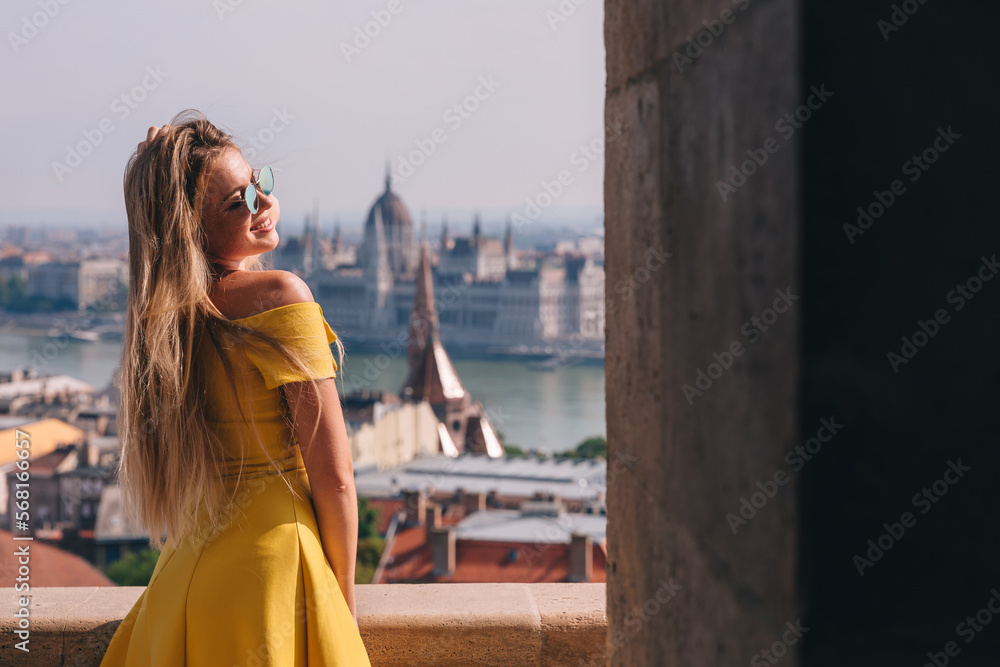 A happy female student enjoys a great view of the Parliament building in the city of Budapest, which is behind her in the background. Europe travel concept
