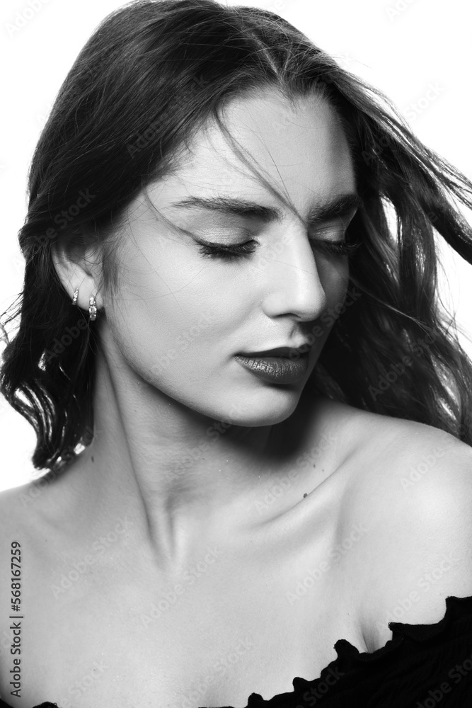 Naklejka premium Fashion and make-up concept. Sensual studio portrait of beautiful brunette woman with long wavy flying hair. Model with closed eyes wearing black blouse. White studio background. Black and white image